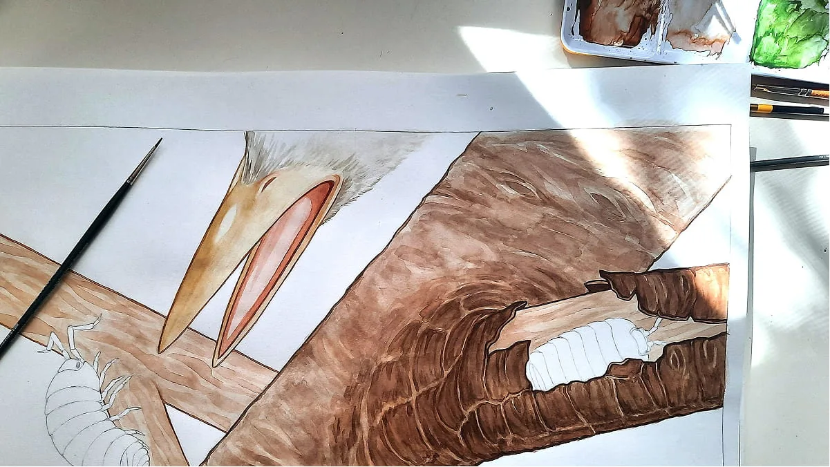 Arbeitsfoto einer Aquarellillustration von Vogelschnabel und Baumrinde mit Assel, umgeben von Pinseln und Farbnäpfen