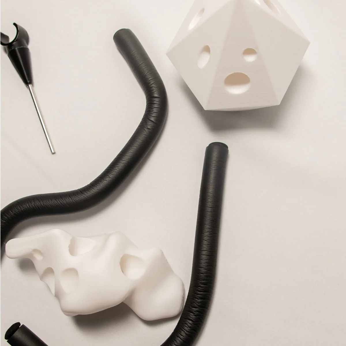 3D-gedruckte weiße Formkörper mit Löchern und schwarze biegsame Schlauchelemente auf hellem Untergrund