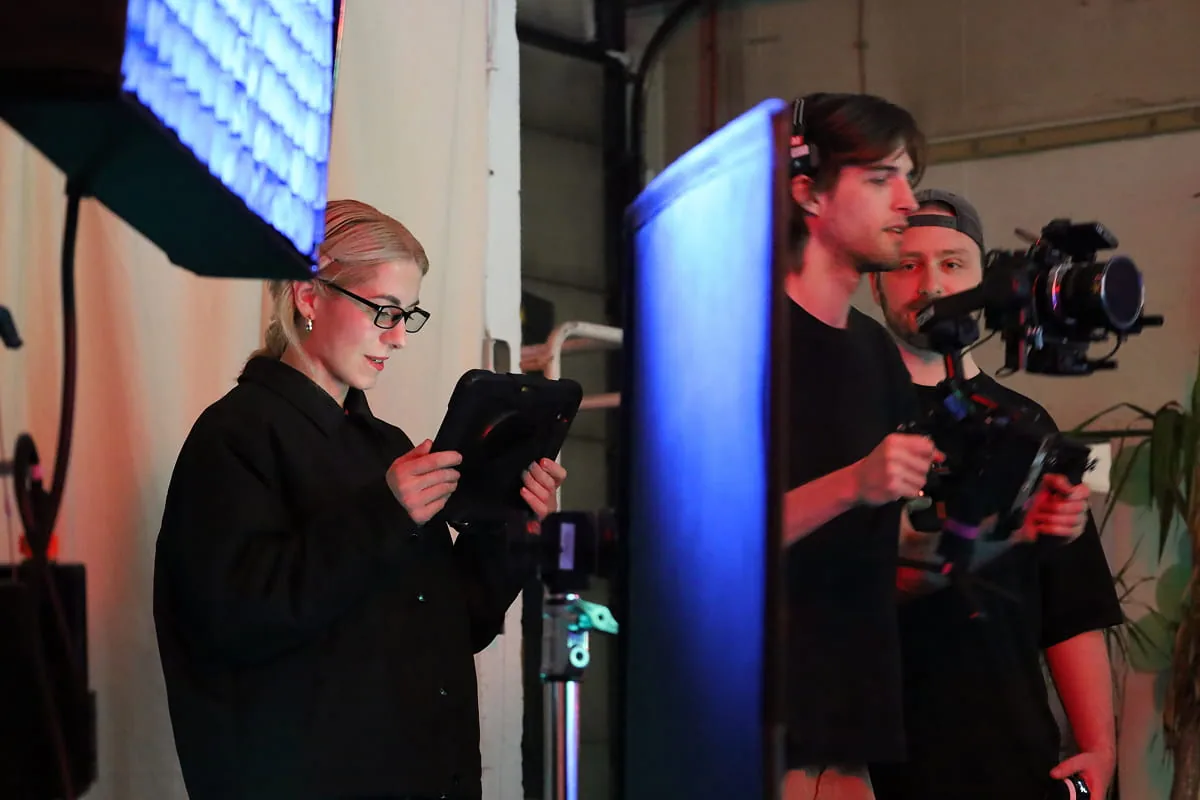 Filmteam am Set mit Kamerakran, Softbox-Licht und einer Person, die den Monitor der Regieassistenz betrachtet