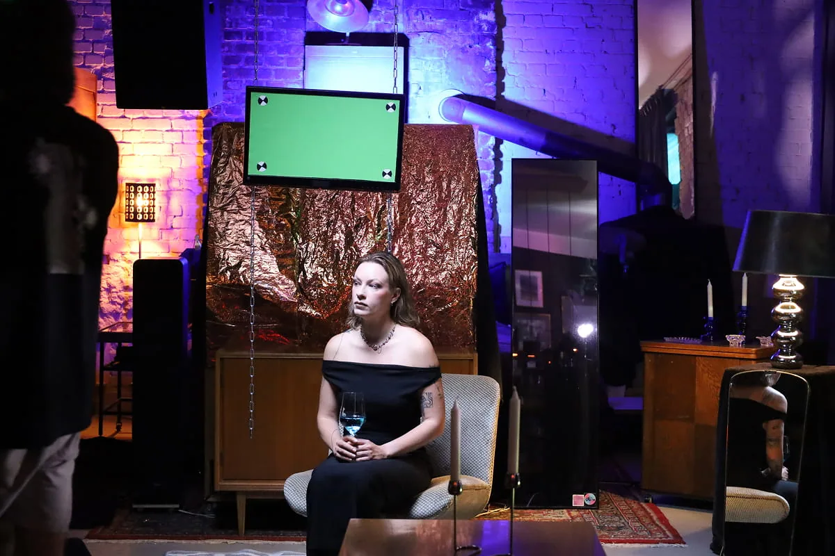 Filmset mit einer sitzenden Frau vor grüner Leinwand, Kupferfolie-Kulisse und violetter Studiobeleuchtung