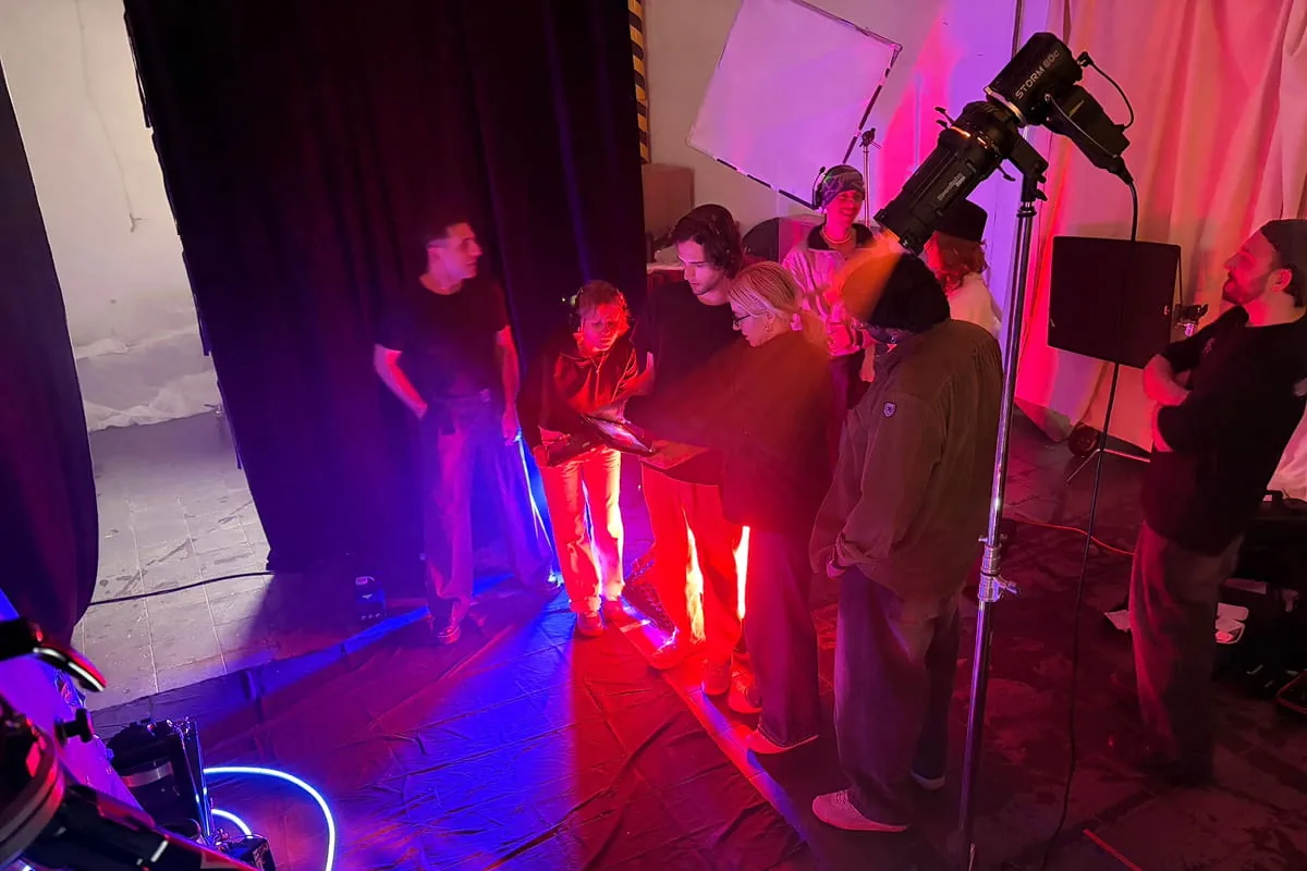 Filmcrew begutachtet gemeinsam eine Kamera im rot-blau beleuchteten Studio zwischen Vorhängen und Lichtreflektoren