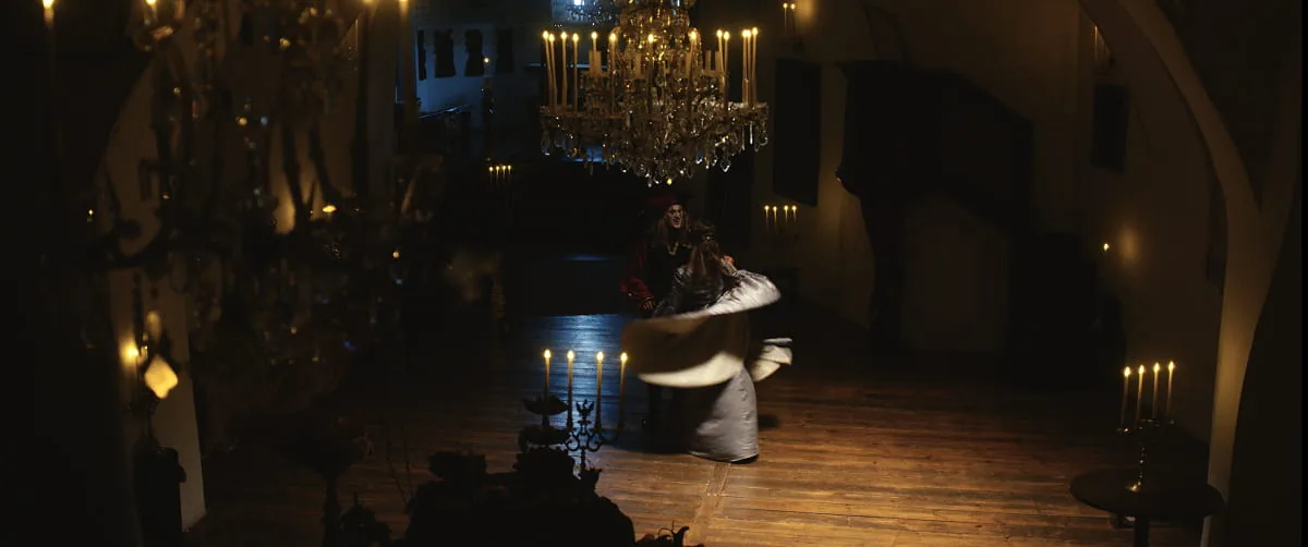 Filmszene in einem kerzenerleuchteten Saal mit Kronleuchter, in dem eine Person in historischem Kostüm sich tanzend dreht