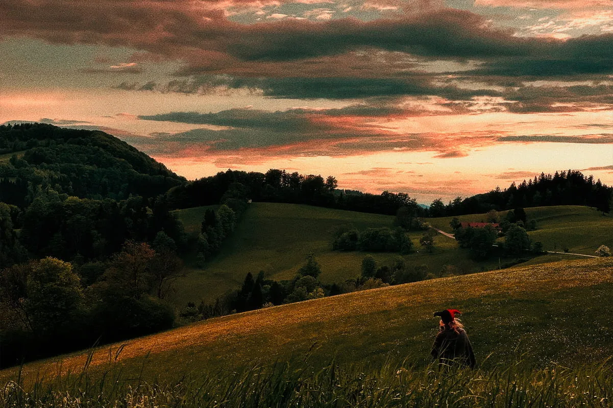 Silhouette einer Person mit Narrenhut in weiter Graslandschaft bei dramatischem Abendhimmel